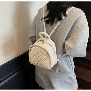 Detail of cream quilted mini backpack with rhinestone decor on model in an indoor setting