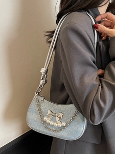 Light blue sequin crescent underarm bag with silver bow and pearl accents on grey suit