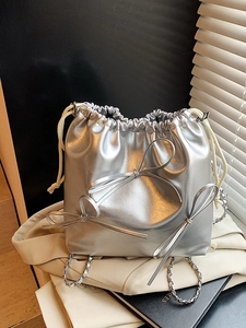 Metallic silver bucket bag with bow accents and chain strap in a lifestyle setting