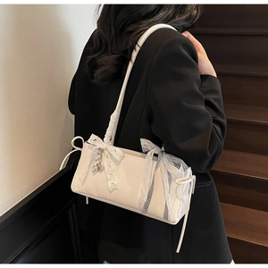 Close-up of cream white rectangular shoulder bag with lace bow and metal heart charm