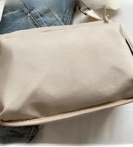 Close-up of beige nylon crossbody bag with smooth metal zipper and textured fabric detail