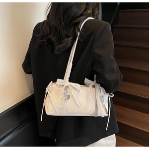 Detail of white lychee leather bag with lace bow and heart charm worn on shoulder