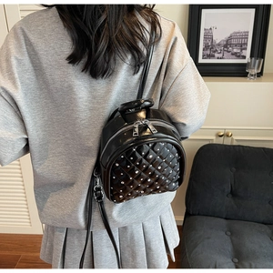 Rear view of model wearing a black quilted mini backpack with silver rivet details