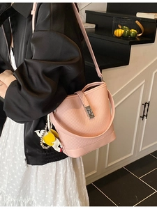 Light pink woven bucket bag with silver buckle and bird charm worn by a model