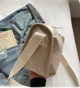 Detail view of beige nylon crossbody bag with wide strap and zipper on casual background