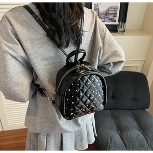 Detailed view of black quilted mini backpack with silver rivets on a woman's back