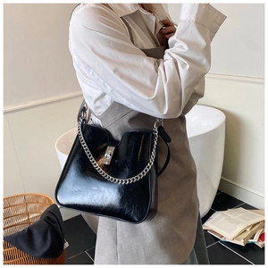 Detail of glossy black leather bucket bag with chunky silver chain on model