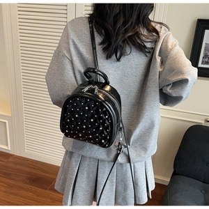 Close-up of black quilted mini backpack with silver rivets worn by a model