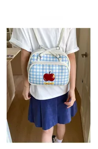 Close-up of blue and white checkered backpack featuring a red apple patch and yellow label
