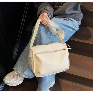 Detail of beige canvas shoulder bag featuring adjustable wide strap and dual zipper pockets