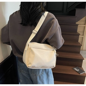 Detail of adjustable canvas messenger bag strap and front zipper pocket in off-white
