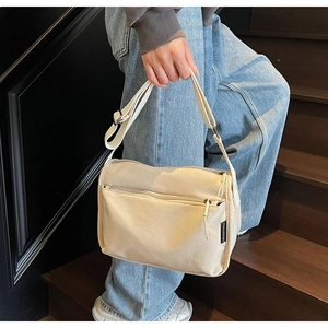 Detail view of beige canvas crossbody bag with multiple zippers and adjustable strap
