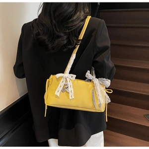 Close-up of a yellow pebbled leather handbag featuring white lace bows and a heart pendant