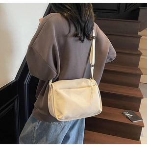 Detail view of cream canvas crossbody bag with adjustable strap and multiple zipper pockets
