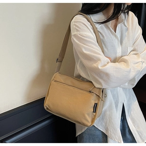Detail of khaki canvas crossbody bag with front zipper pocket and adjustable strap