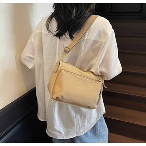 Rear view of a beige canvas crossbody bag with adjustable wide strap on a model