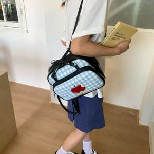 Detail of blue gingham tote bag featuring red apple embroidery and black leather straps