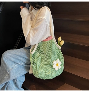 Detail of green mesh tote bag featuring a white crochet daisy on a woven texture