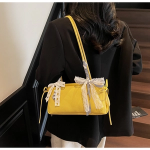 Detail of yellow pebbled leather bag with white lace bow and checkered ribbon accent