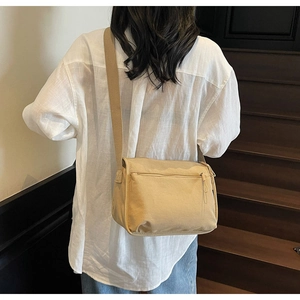 Rear view of a casual beige canvas crossbody bag with adjustable wide strap on a model