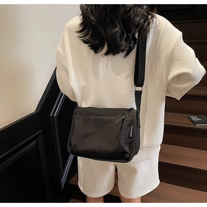 Side view of black nylon crossbody bag with wide strap and CHUANGMI brand tag