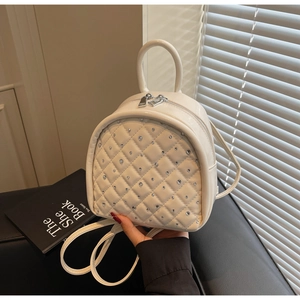 Detail of quilted beige mini backpack featuring sparkling rhinestone studs and top handle