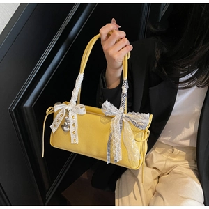Detail of yellow pebbled leather crossbody bag with lace bows and heart pendants