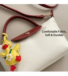 Detail of crossbody bag with cream fabric, maroon leather handles and yellow duck charm