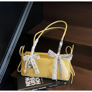 Macro shot of yellow leather bag with lace bow, ribbon, and silver heart charm detail