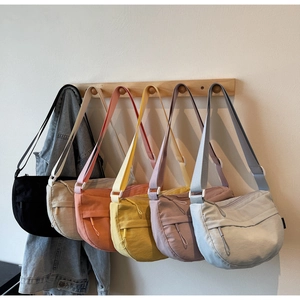Detail view of nylon crossbody bags in six vibrant colors hanging on a wooden rack