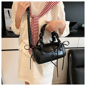 Detail der schwarzen Handtasche mit gerafftem Griff und Zierbändern an einem Model