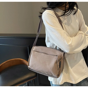 Detail view of khaki canvas crossbody bag featuring front zipper and woven logo tag