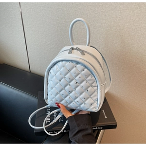 Macro detail of a light blue quilted mini backpack with rhinestone studs on a book