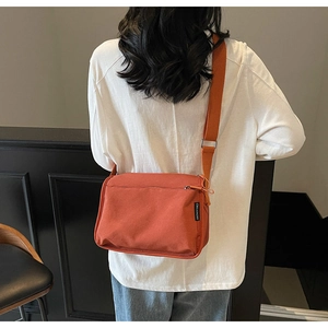 Detail of orange nylon crossbody bag with adjustable wide strap and side brand label