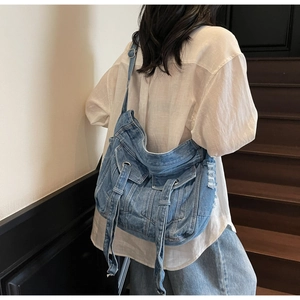 Detailed view of the denim crossbody bag with metallic eyelets and frayed edges on model