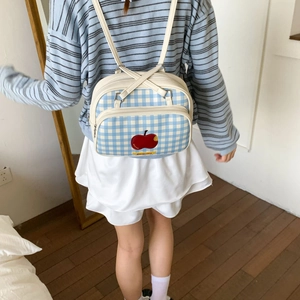 Detail of blue plaid tote bag showing the apple embroidery and adjustable strap on a model