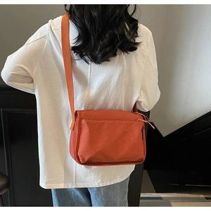 Rear view of orange crossbody bag showing functional back zipper pocket and wide strap