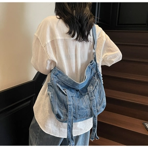 Detail of blue denim crossbody bag featuring utility pockets and metallic ring buckles