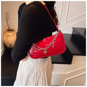 Detail of red glossy patent leather shoulder bag with silver chains and heart charm on model