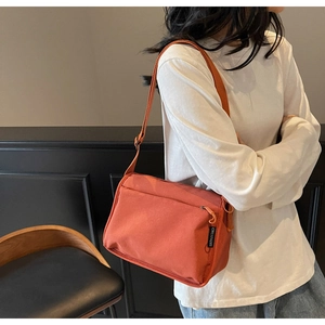 Detail of brick orange canvas crossbody bag with front zipper and Chuangmi woven label