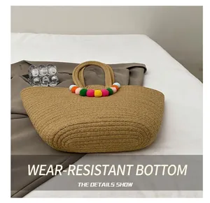 Détail de la base durable de ce sac cabas en paille avec des pompons colorés sur la poignée