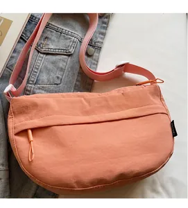 Detail of orange nylon crossbody bag with adjustable pink strap on a bed setting