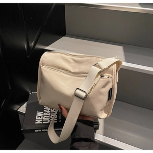 Detail view of cream canvas crossbody bag with multiple zippers on dark stairs
