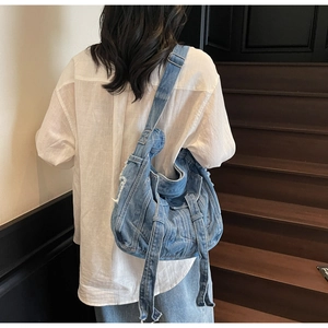 Detail of light blue washed denim crossbody bag featuring frayed edges and tassels
