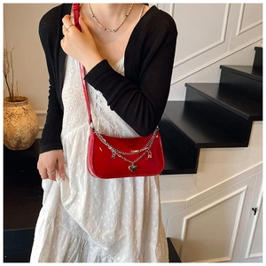 Detail of red patent leather crossbody bag with silver chains and heart charms