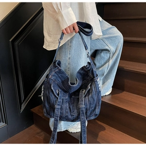 Detail of distressed dark blue denim crossbody bag featuring jacket pocket elements