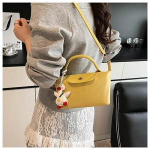 Detail of yellow leather dumpling handbag featuring a plush duck pendant and flap cover