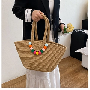 Gros plan du sac cabas en paille tressée avec pompons colorés et texture tissée à la main
