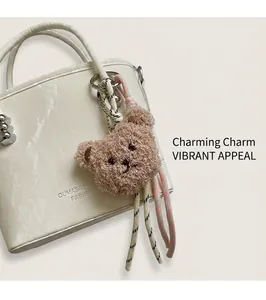 Detail of plush teddy bear charm with woven tassels attached to a white bucket bag