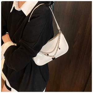 White glossy patent leather shoulder bag with silver chains and heart charms on model